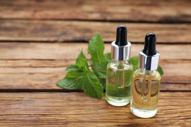 Photo of Bottles of essential oil and mint on wooden table, closeup. Space for text