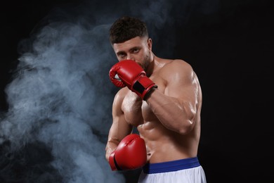 Man wearing boxing gloves in smoke on black background. Space for text