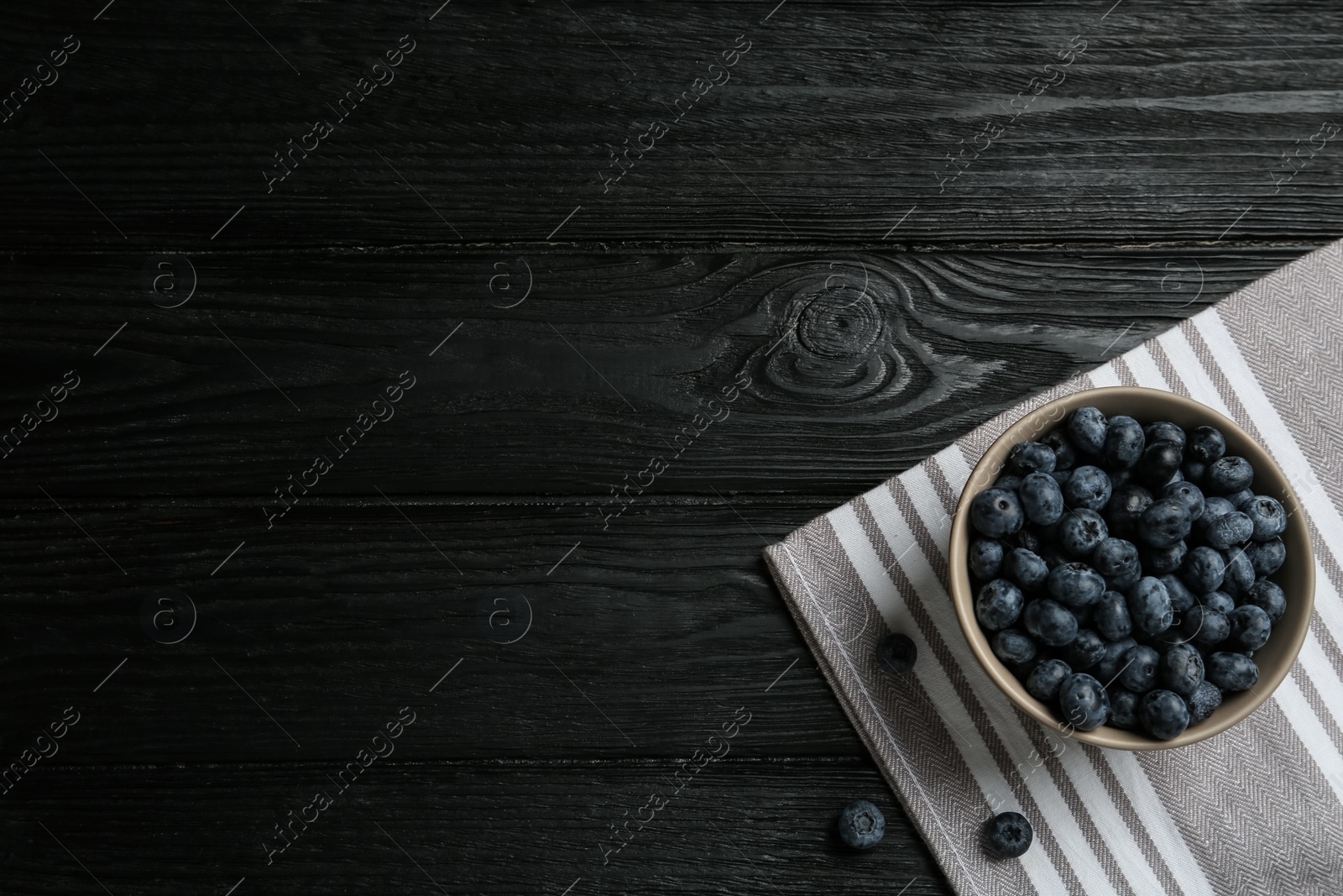 Photo of Ceramic bowl with blueberries on black wooden table, flat lay and space for text. Cooking utensil