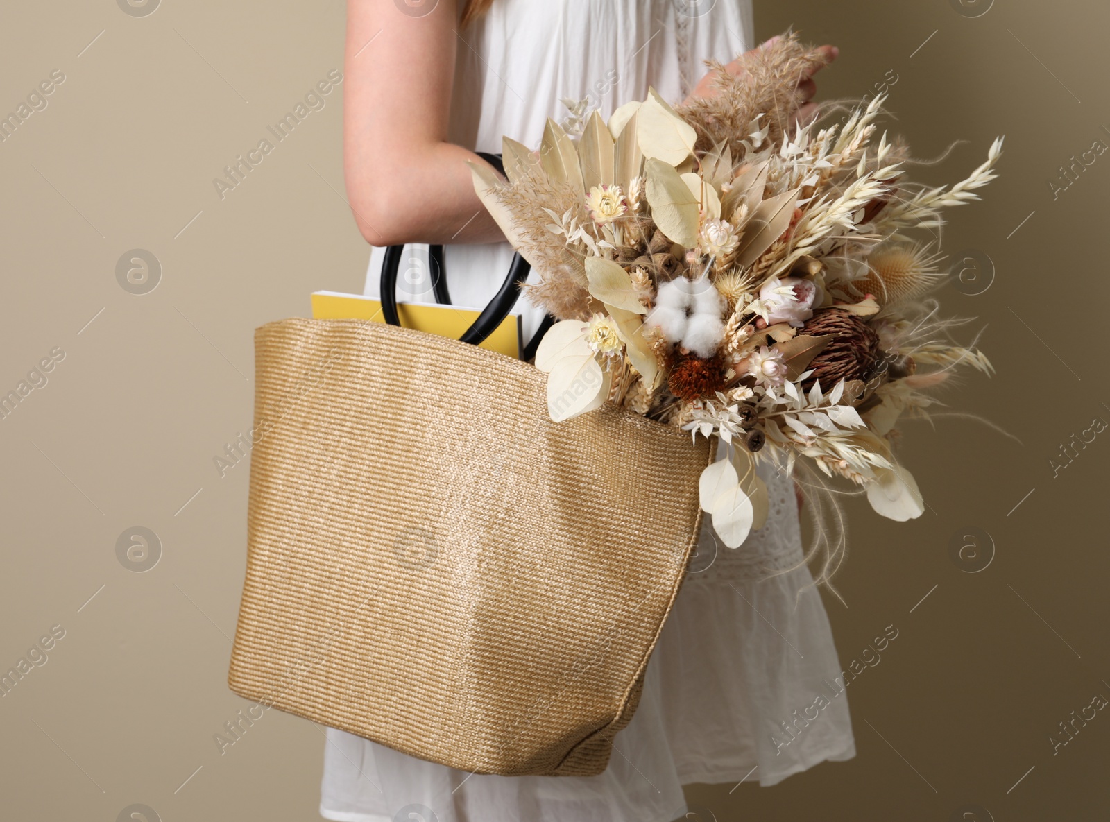 Photo of Woman holding beach bag with beautiful bouquet of dried flowers on beige background, closeup