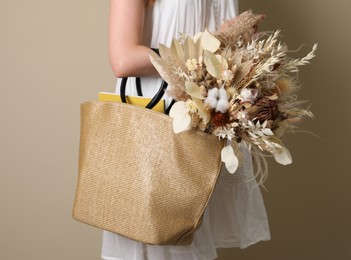 Woman holding beach bag with beautiful bouquet of dried flowers on beige background, closeup
