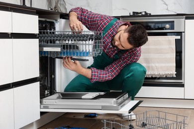 Serviceman repairing dishwasher cutlery rack in kitchen