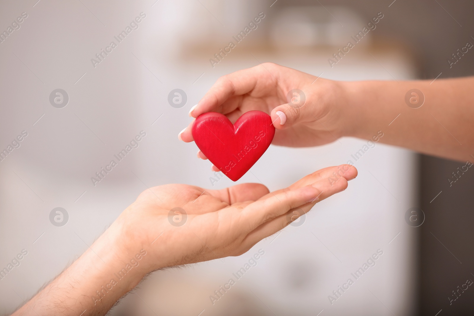 Photo of Man giving red heart to woman on blurred background, closeup. Donation concept