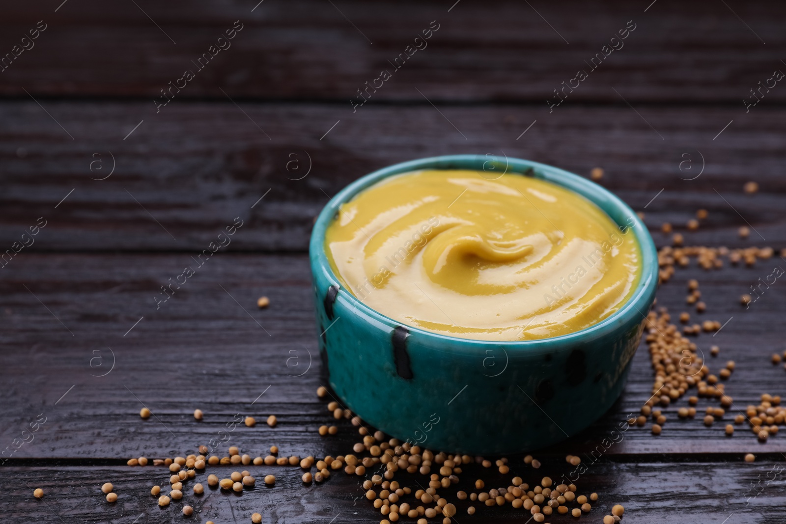 Photo of Sauce bowl with delicious mustard and seeds on dark wooden table, closeup. Space for text