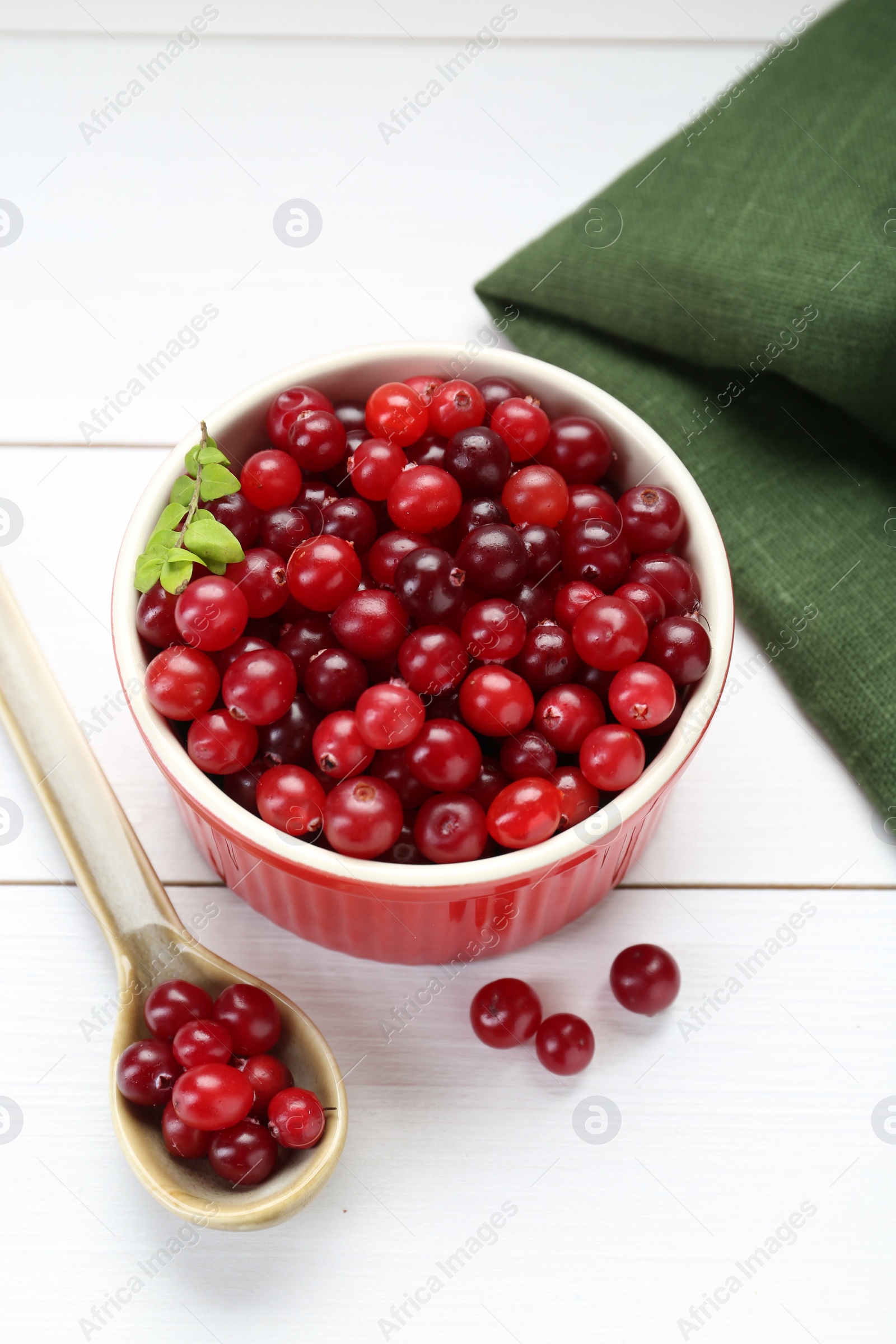 Photo of Fresh ripe cranberries in bowl and spoon on white wooden table, above view