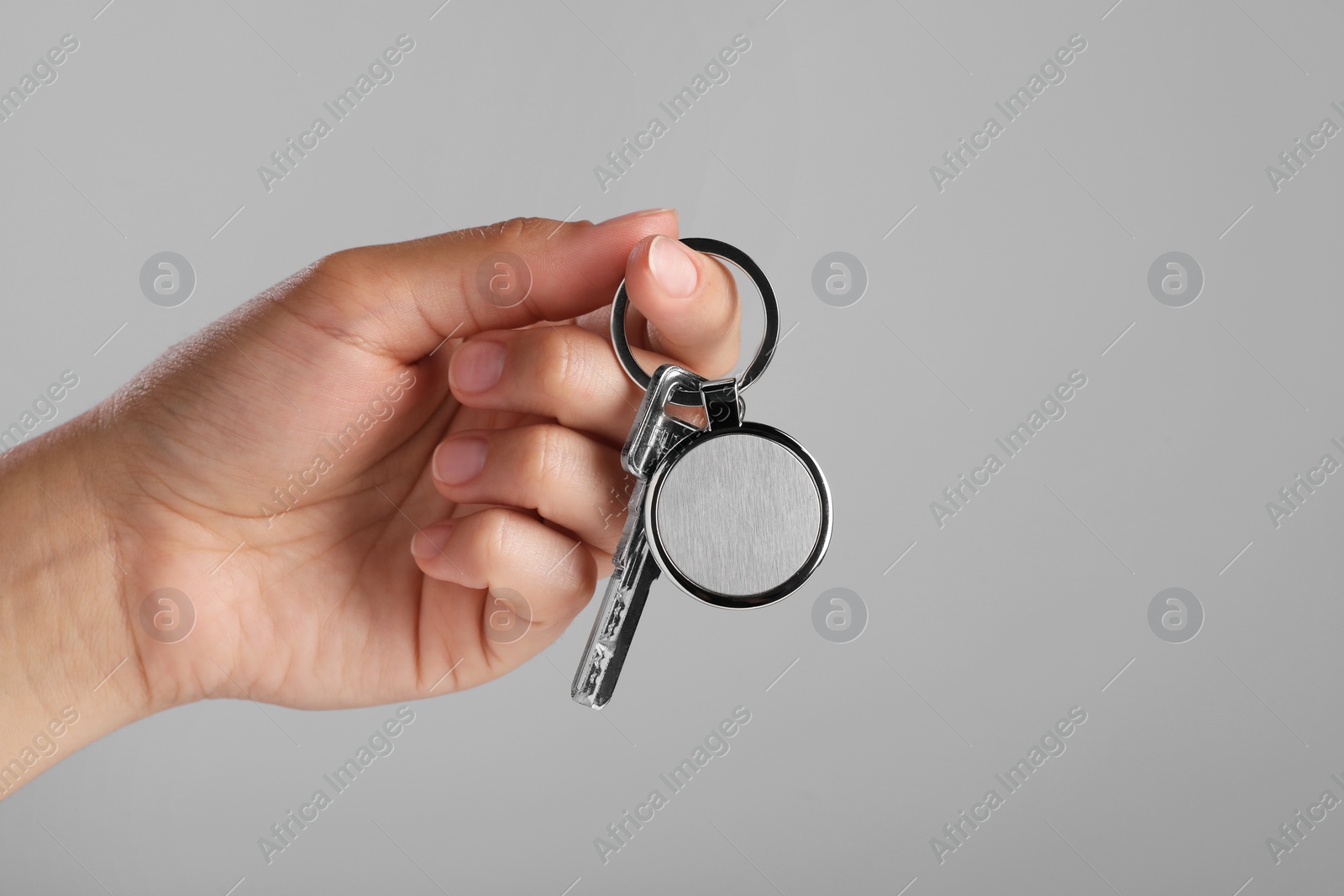 Photo of Woman holding key with metallic keychain on grey background, closeup. Space for text