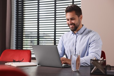 Photo of Happy young man working on laptop at table in office