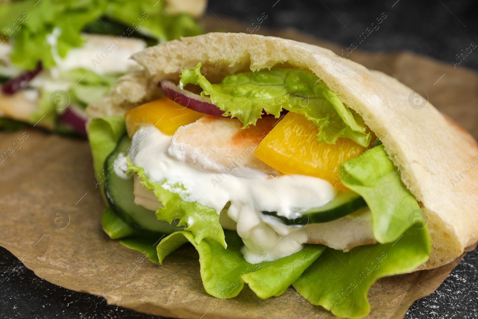 Photo of Delicious pita sandwich with chicken breast and vegetables on parchment paper, closeup