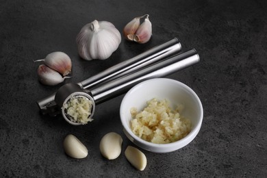 Photo of Garlic press, cloves and mince on grey table. Kitchen utensil