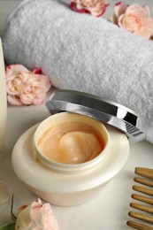 Photo of Open jar of hair care cosmetic product, comb and towel on white table