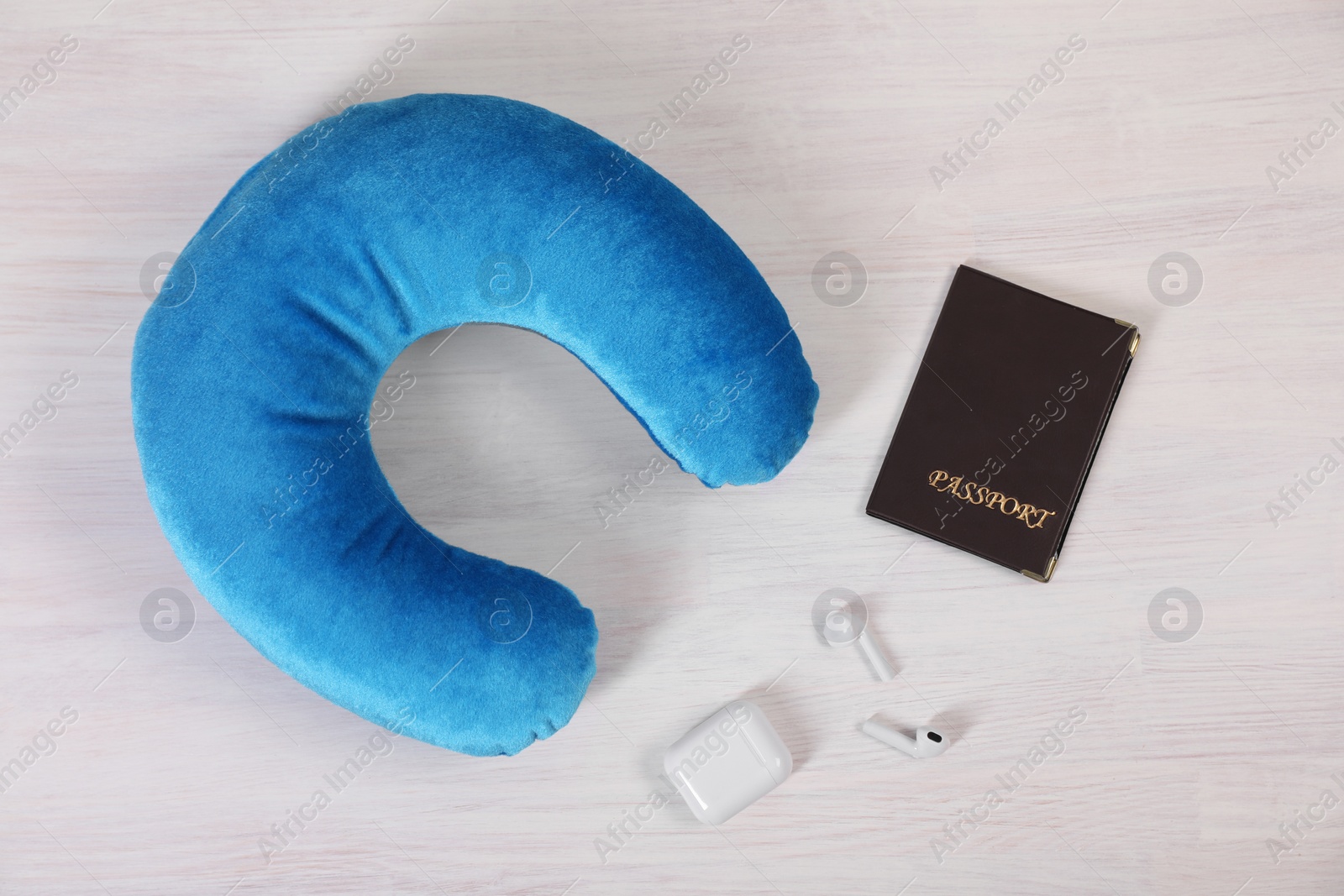 Photo of Light blue travel pillow, passport and earphones on white wooden background, flat lay