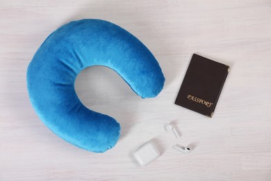 Photo of Light blue travel pillow, passport and earphones on white wooden background, flat lay