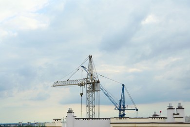 Photo of Construction site with tower cranes near building under cloudy sky