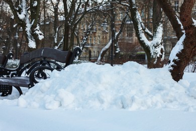 Pile of snow, trees and bench in winter park