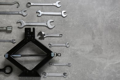 Photo of Car scissor jack and wrench set on grey surface, flat lay. Space for text