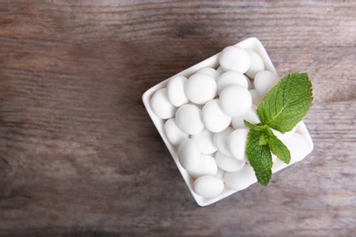 Photo of Bowl with tasty mint candies and leaves on wooden background, top view