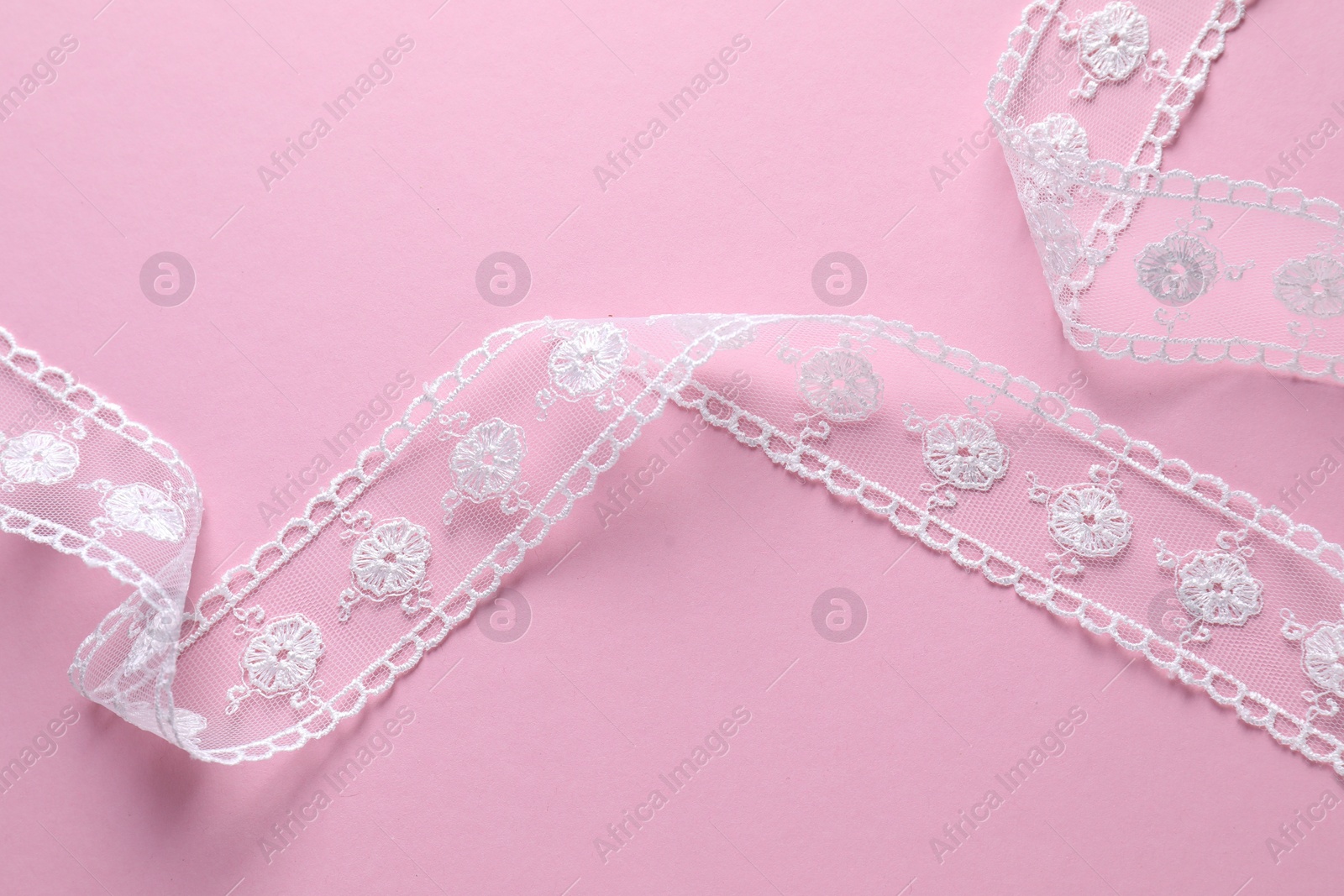 Photo of White lace ribbon on pink background, top view