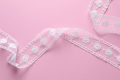 White lace ribbon on pink background, top view