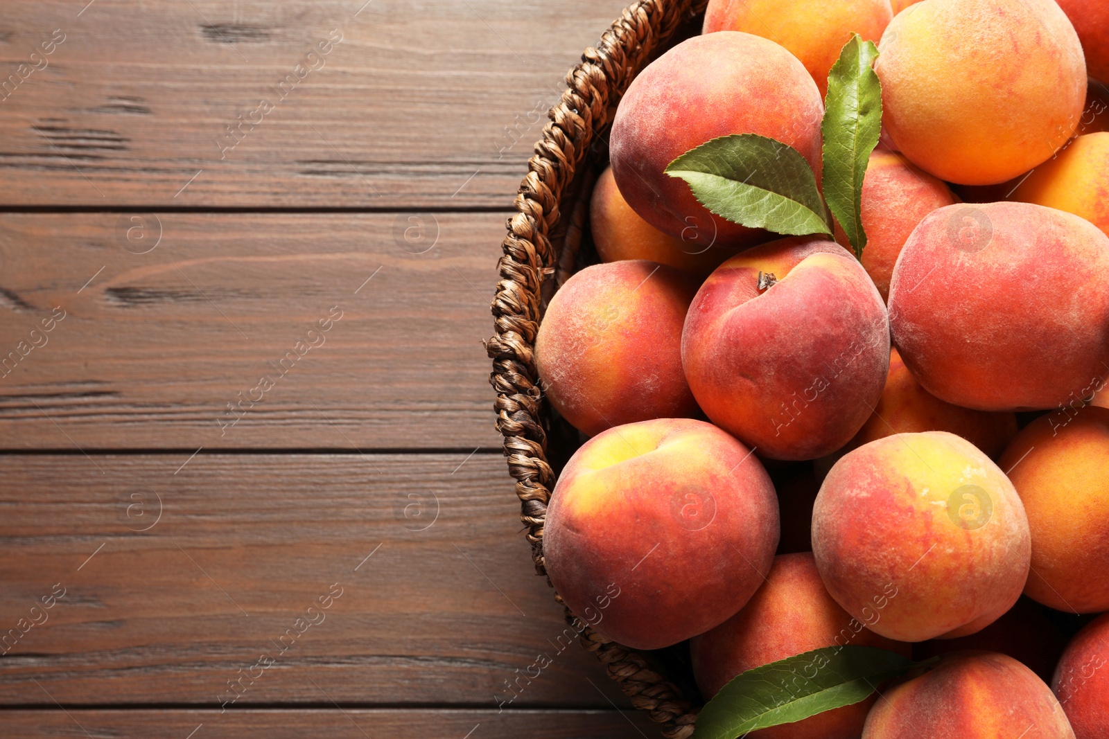 Photo of Wicker basket with fresh sweet peaches on wooden table, top view