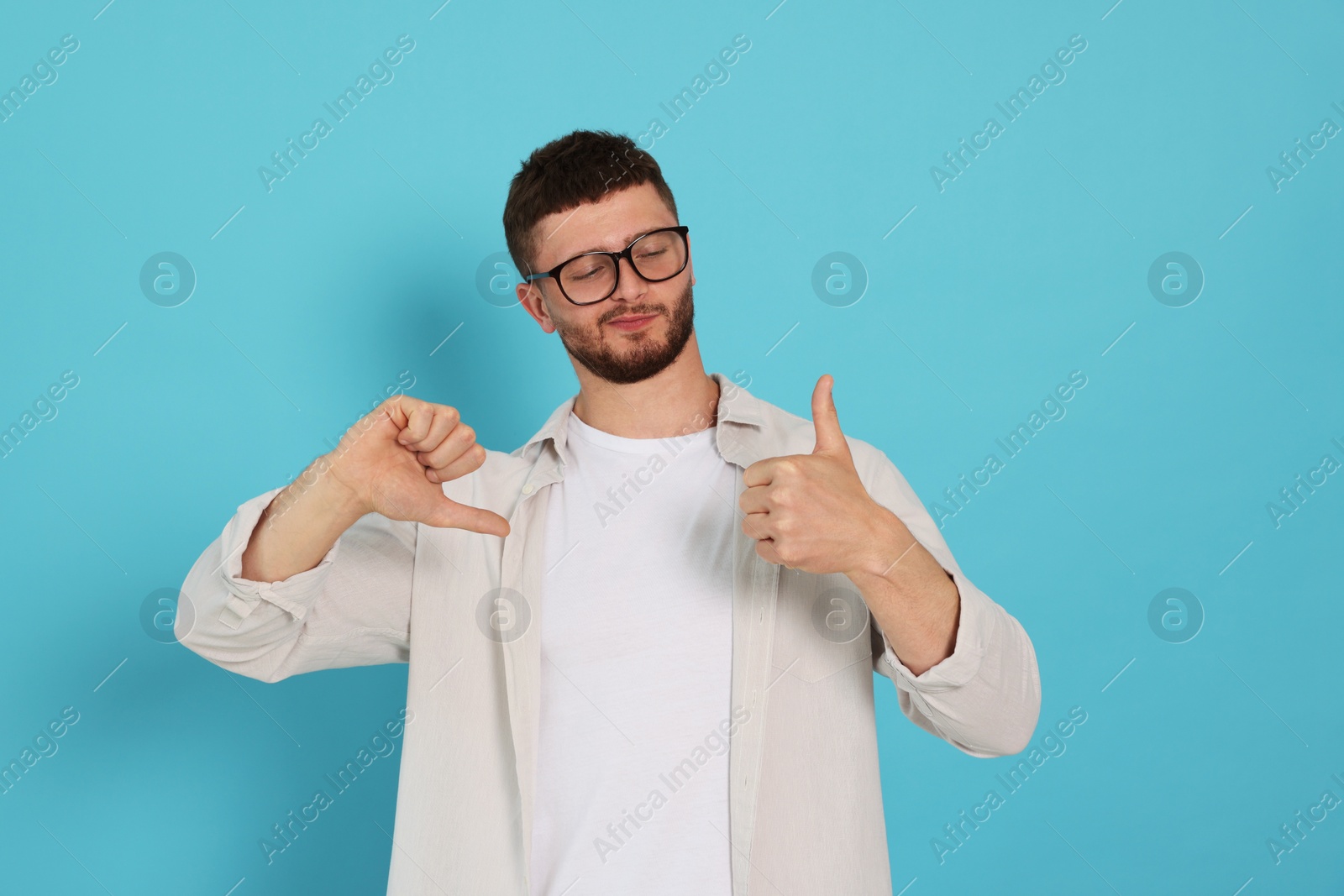 Photo of Young man showing thumbs up and down on light blue background