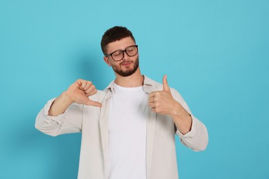 Young man showing thumbs up and down on light blue background