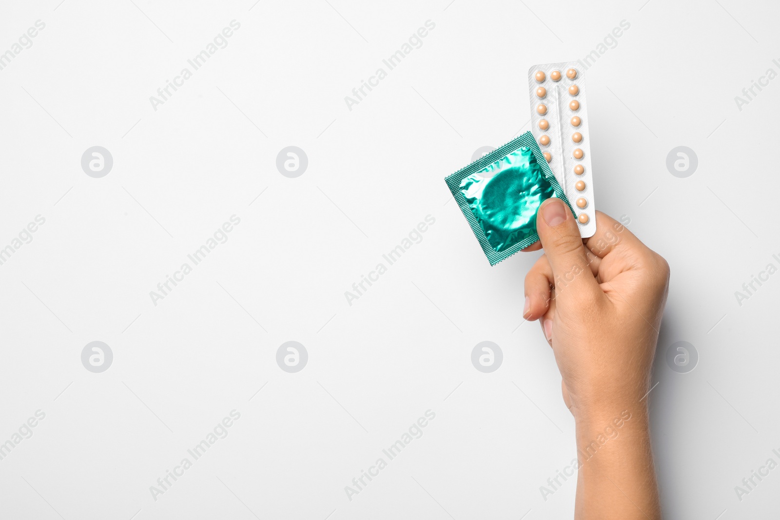 Photo of Woman holding condom and birth control pills on white background, top view. Safe sex