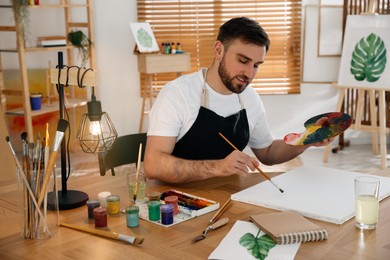 Photo of Young man painting with brush in artist studio