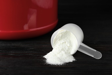 Scoop and scattered protein powder on black wooden table