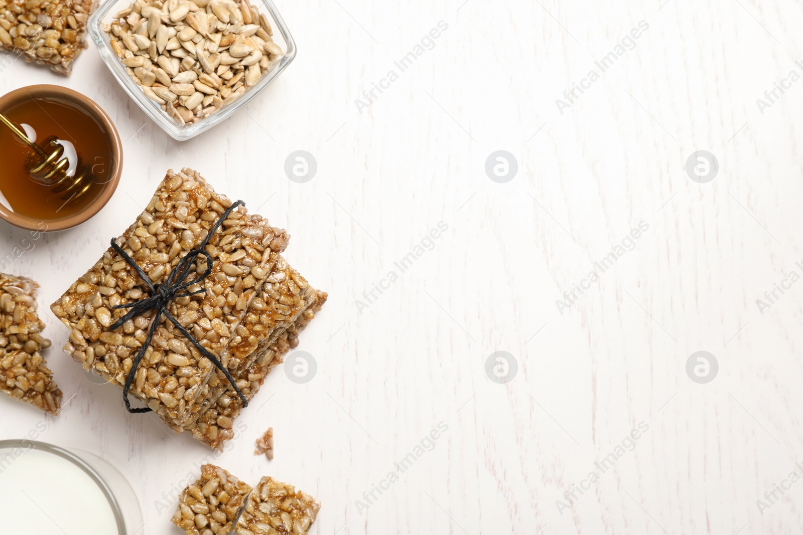 Photo of Delicious sweet kozinaki bars, honey and milk on white wooden table, flat lay. Space for text