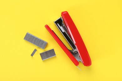 Photo of Red stapler with staples on yellow background, flat lay