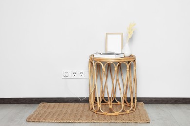 Photo of Rattan table with charging smartphone near white wall, space for text