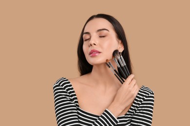 Photo of Beautiful woman with different makeup brushes on light brown background