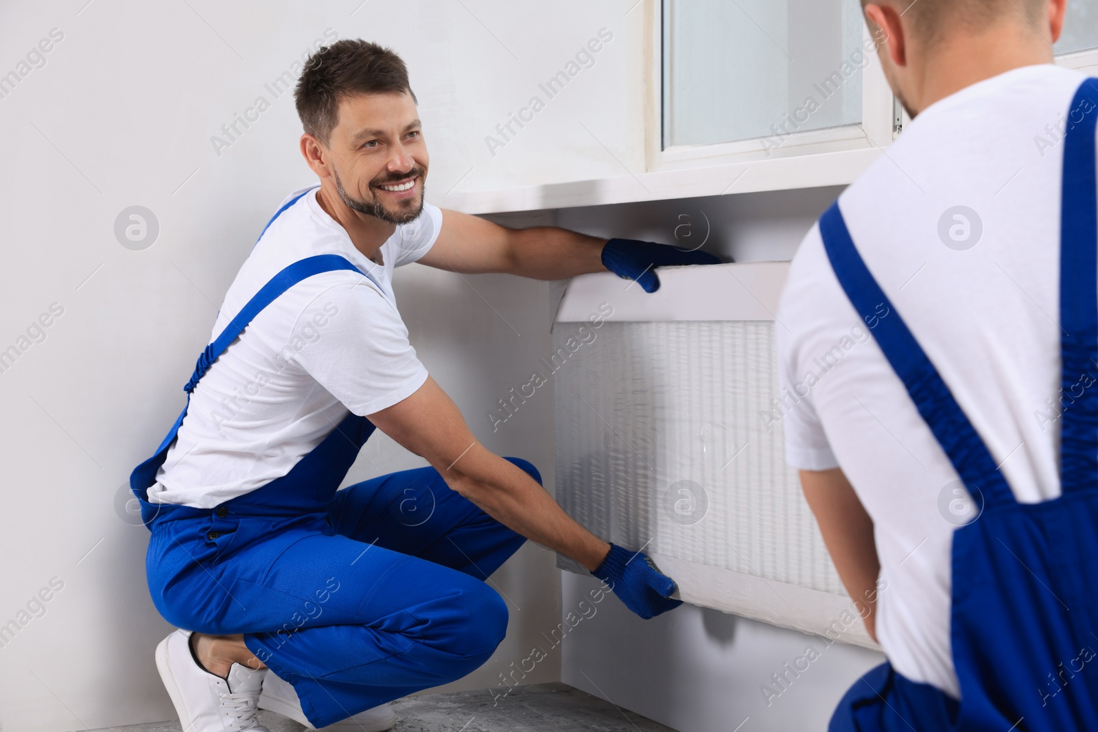 Photo of Professional plumbers installing new heating radiator in room