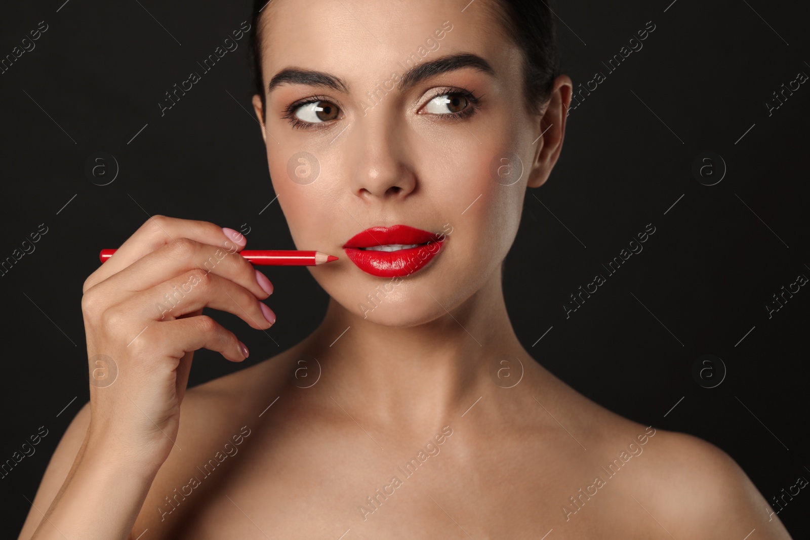 Photo of Pretty young woman with beautiful red lip pencil on black background