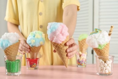 Photo of Woman holding waffle cone with cotton candy indoors, closeup