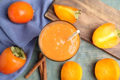 Photo of Tasty persimmon smoothie with straw on light blue wooden table, flat lay