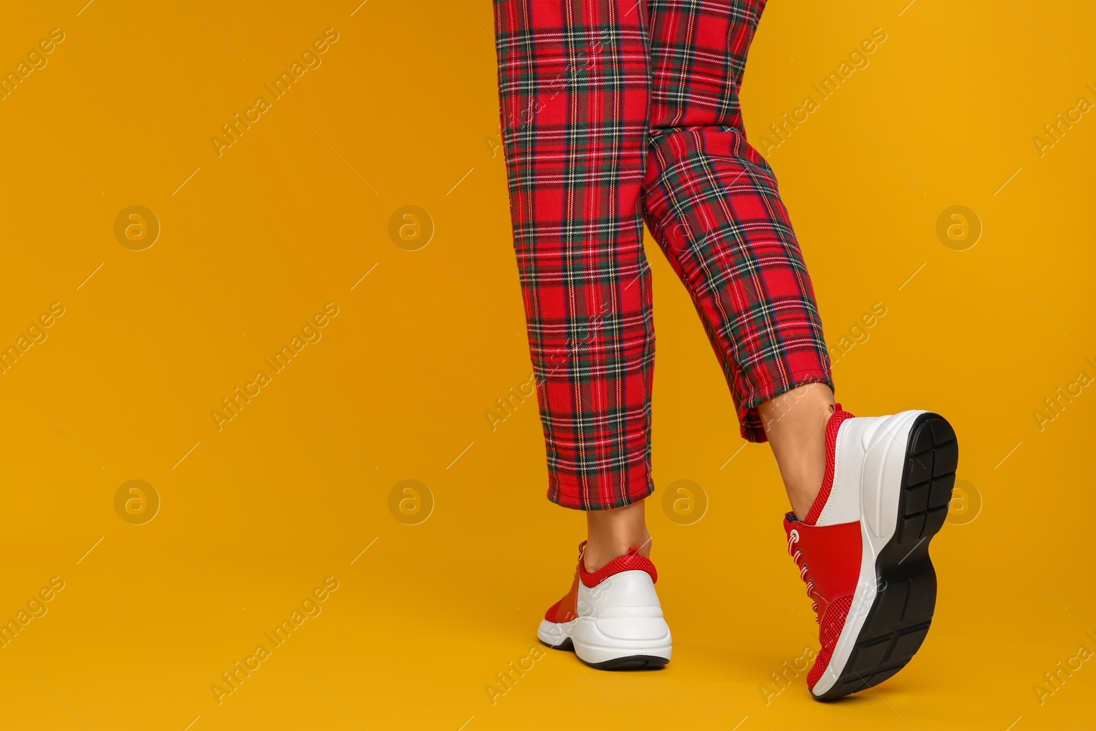 Photo of Woman wearing stylish sneakers on yellow background, closeup. Space for text