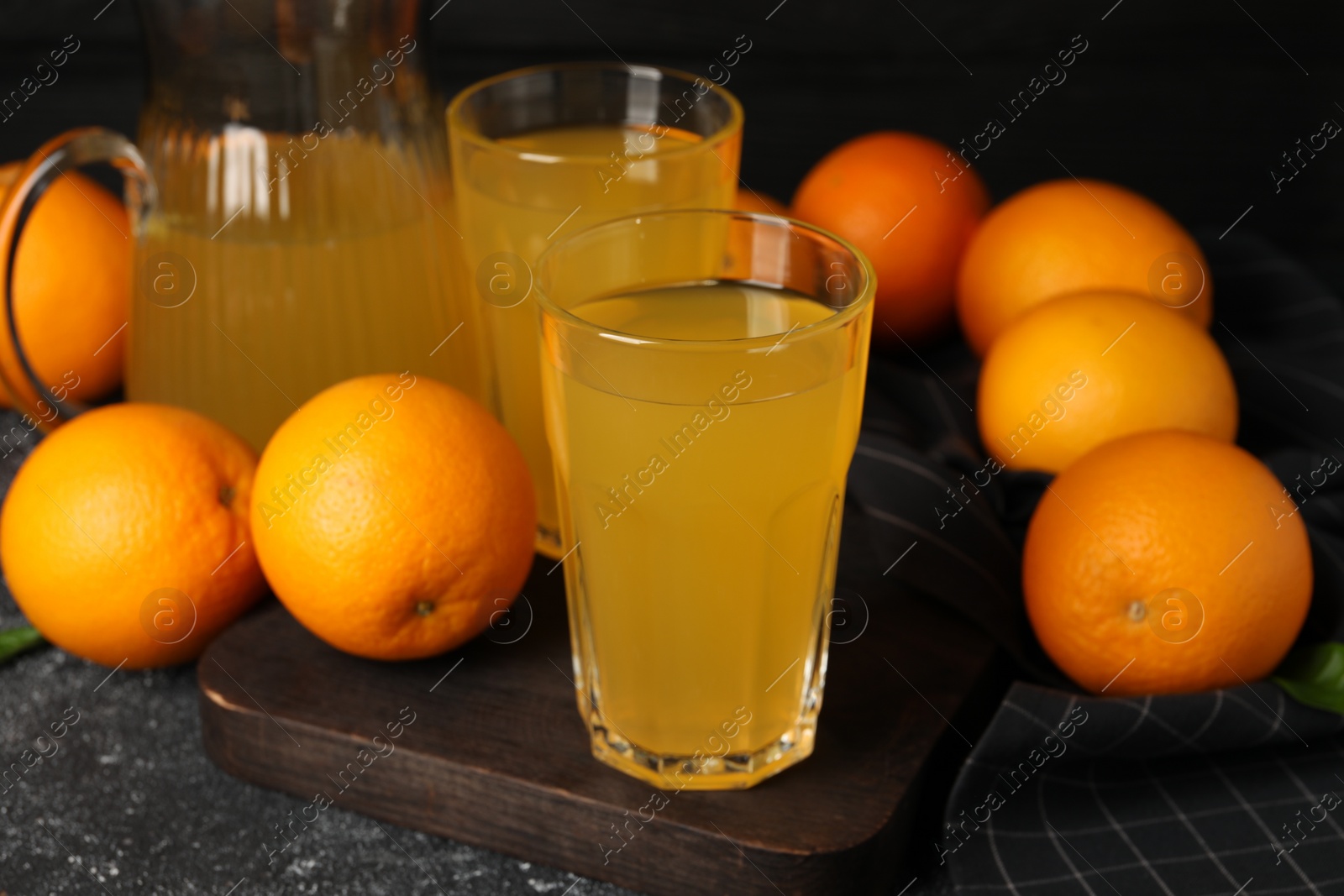 Photo of Many ripe oranges and fresh juice on dark grey table