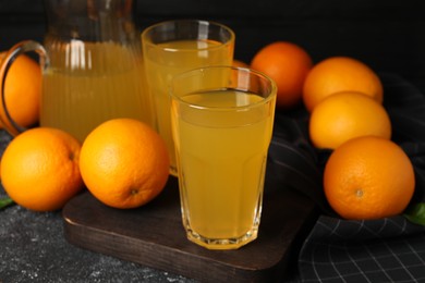 Many ripe oranges and fresh juice on dark grey table