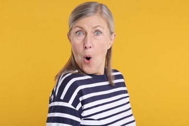 Portrait of surprised senior woman on yellow background