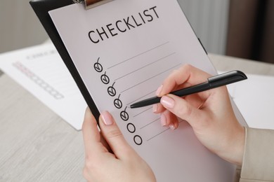 Photo of Woman filling Checklist at wooden table indoors, closeup
