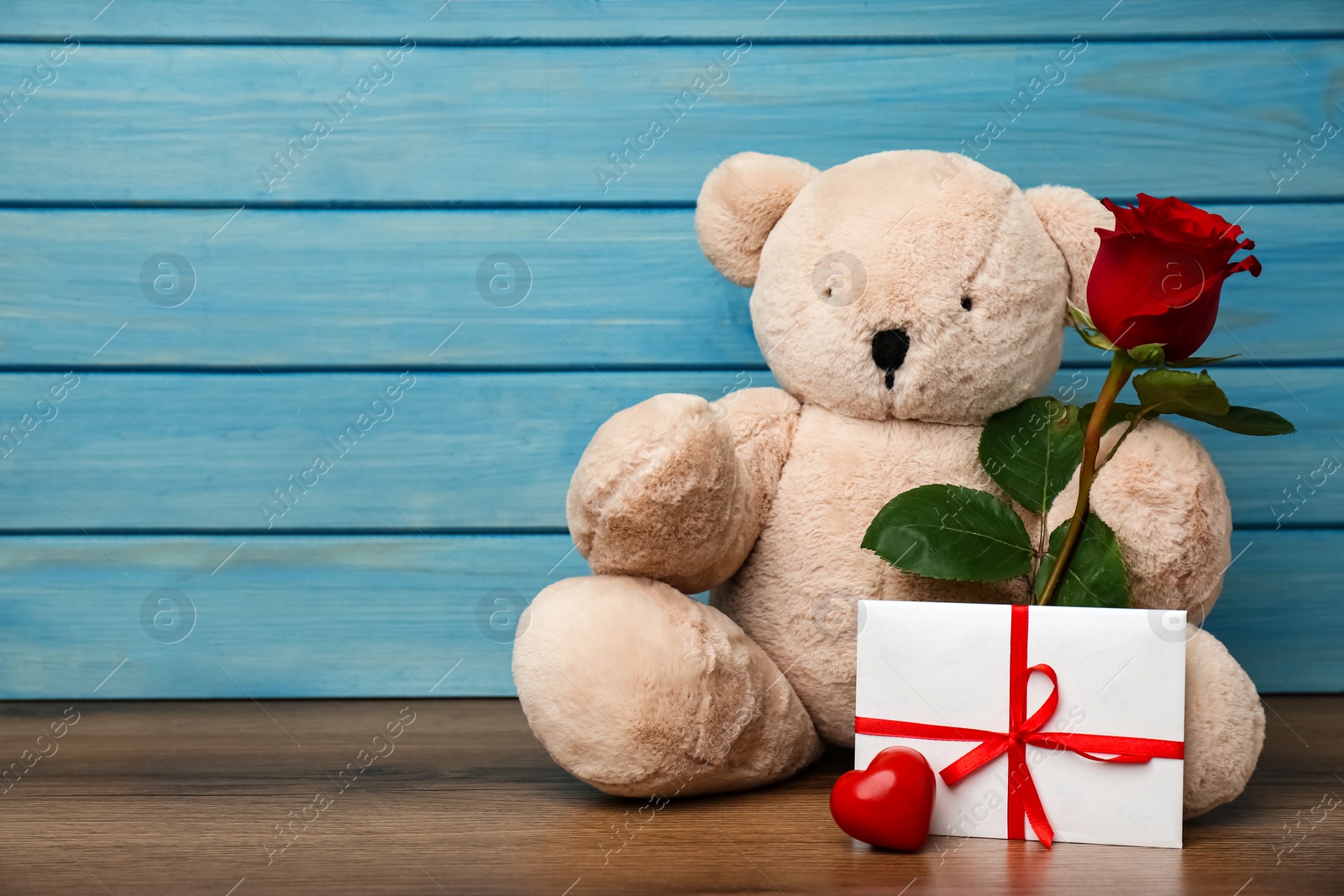 Photo of Cute teddy bear with red heart, envelope and rose on wooden table, space for text. Valentine's day celebration