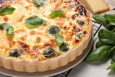 Photo of Delicious homemade quiche with salmon, broccoli and basil leaves on table, closeup