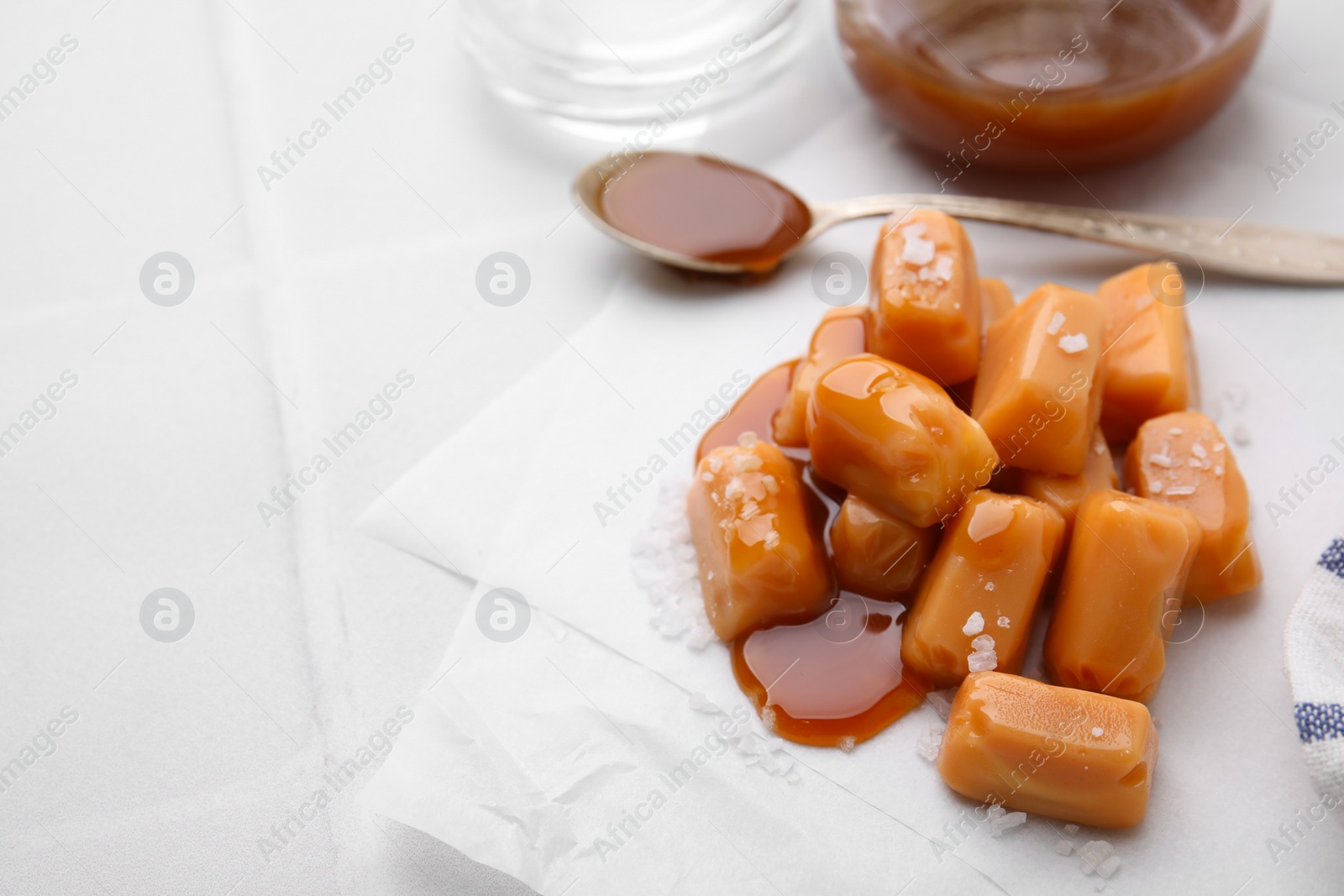 Photo of Yummy caramel candies and sea salt on white table. Space for text