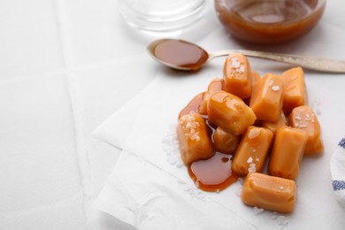 Yummy caramel candies and sea salt on white table. Space for text