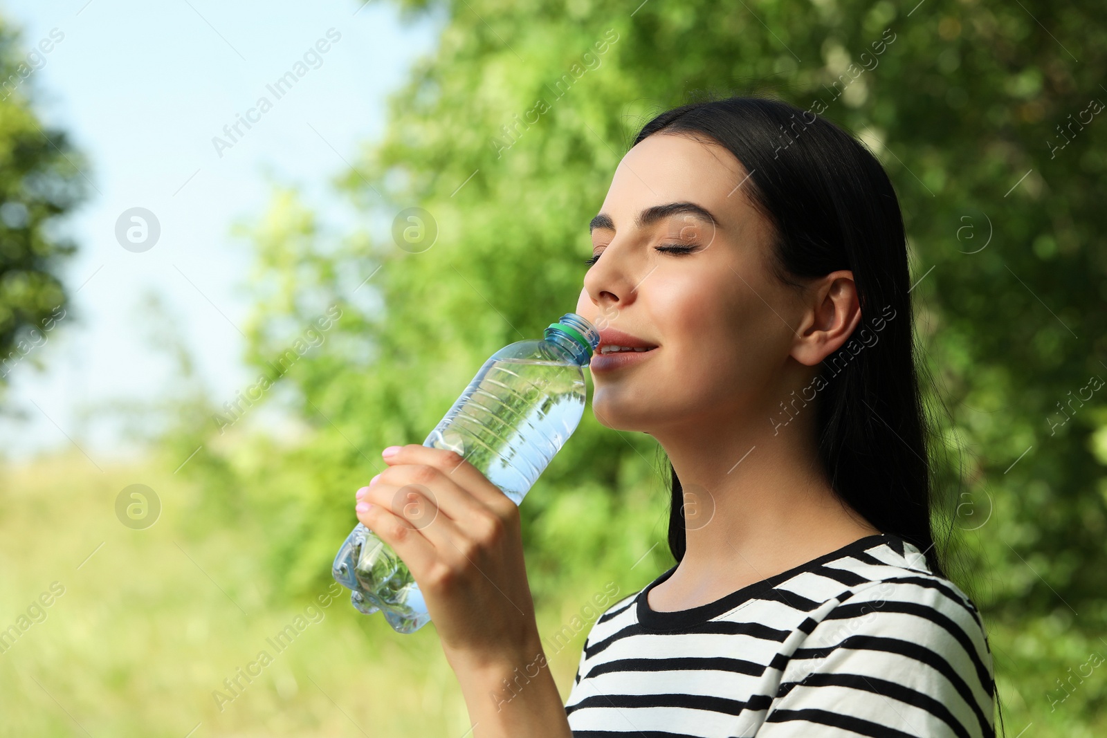 Photo of Young woman drinking water outdoors. Refreshing drink