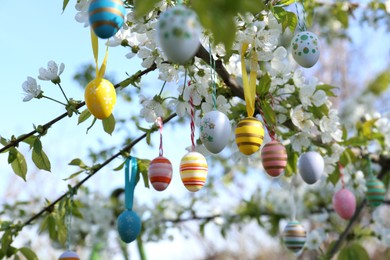 Beautifully painted Easter eggs hanging on blooming tree outdoors, closeup