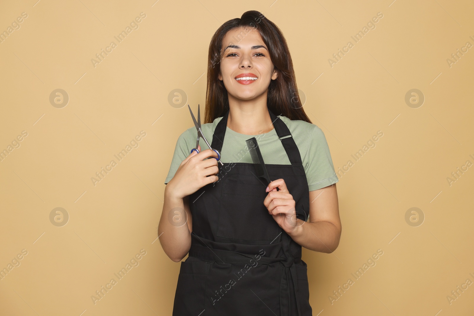 Photo of Portrait of happy hairdresser with professional scissors and comb against pale orange background