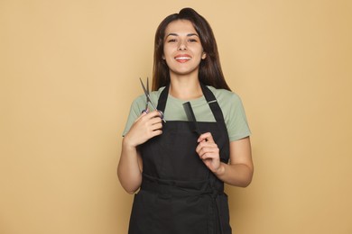 Photo of Portrait of happy hairdresser with professional scissors and comb against pale orange background