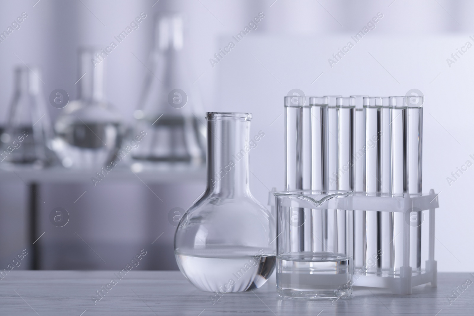 Photo of Different laboratory glassware with transparent liquid on wooden table against blurred background. Space for text